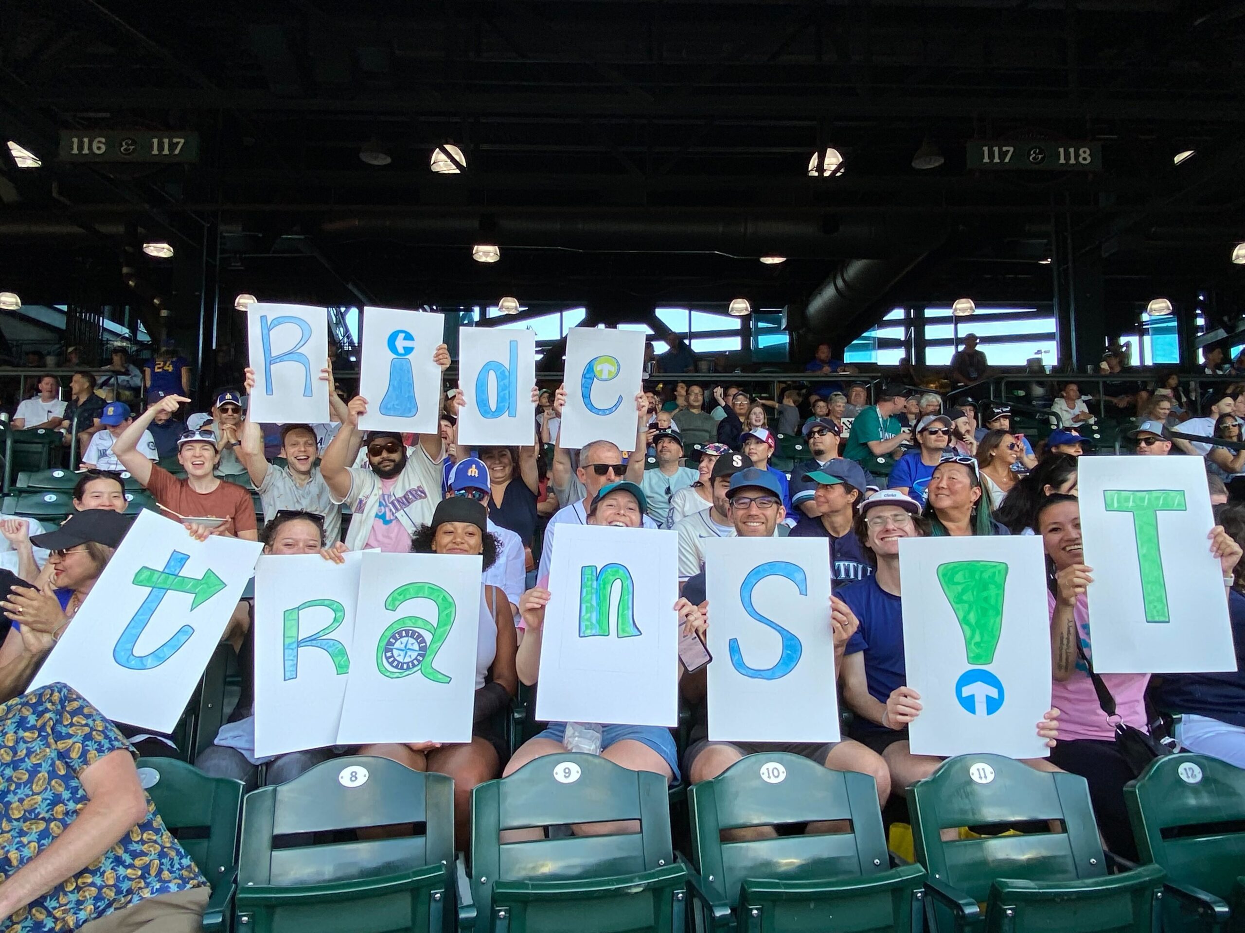 Fans at a Mariners Game holding up signs that read "Ride Transit!"