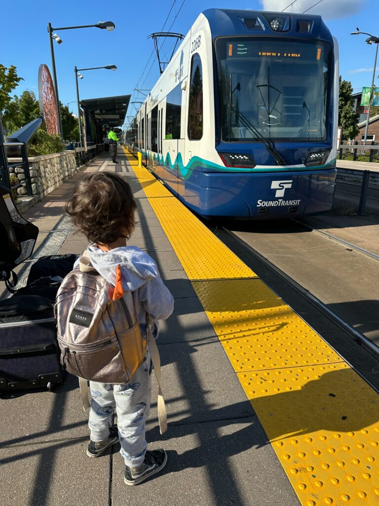 Child wearing a backpack watches the link light rail pull into a station