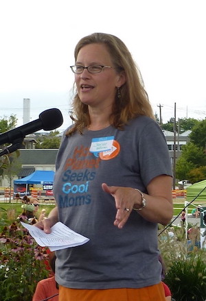 Jemae Hoffman speaks  at a microphone at an outdoor event. 