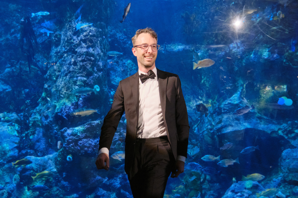 Kirk Hovenkotter stands in front of the giant fish aquarium at Tuxes & Trains.