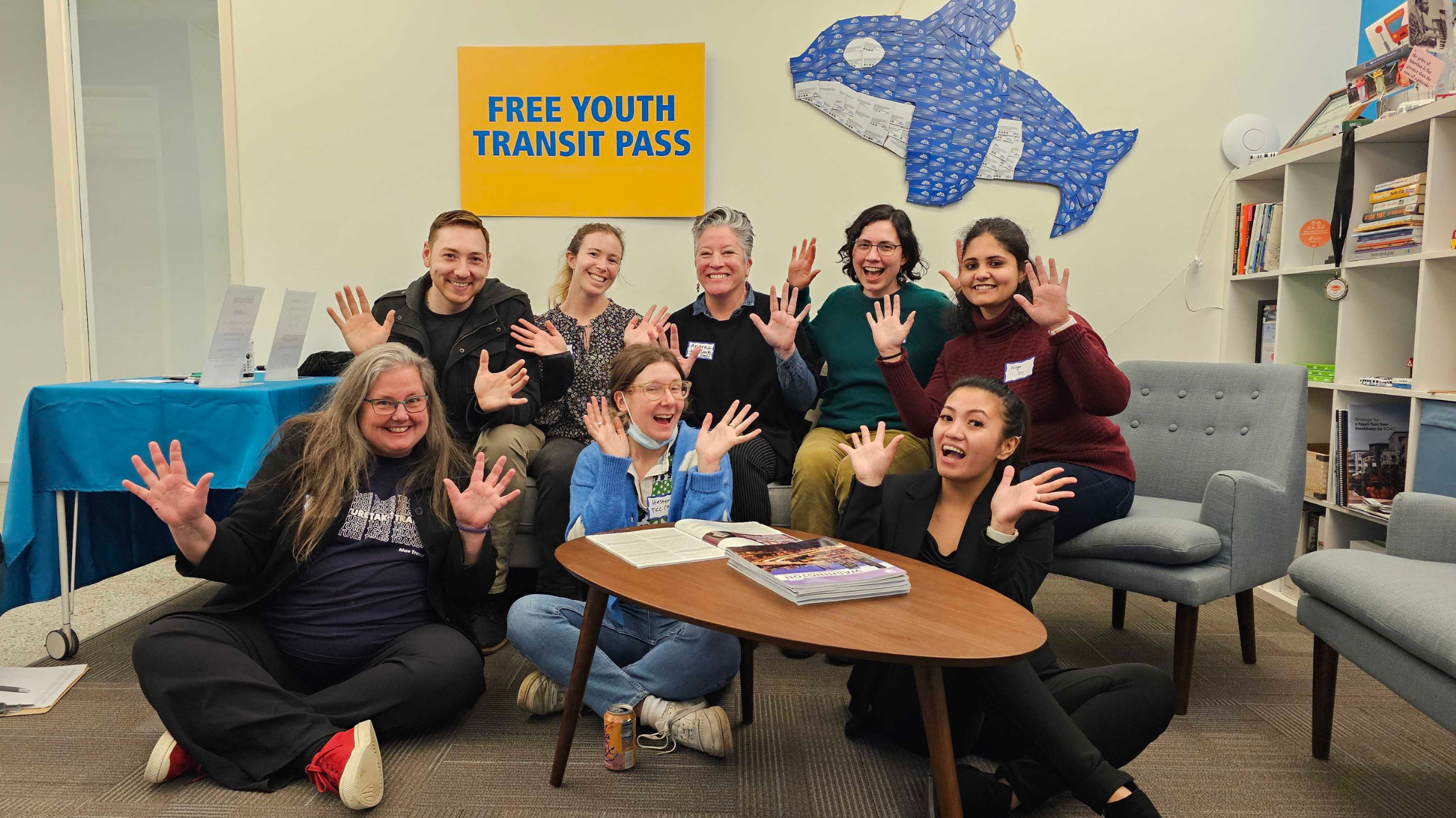 TCC Staff pose beneath a sign that reads "FREE YOUTH TRANSIT PASS" and an Orca made of ORCA cards. 