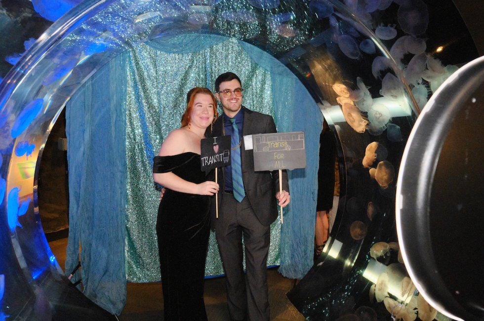 Guests holding pro-transit signs pose for a photo under the jellyfish arch at the Seattle Aquarium at Tuxes & Trains. 