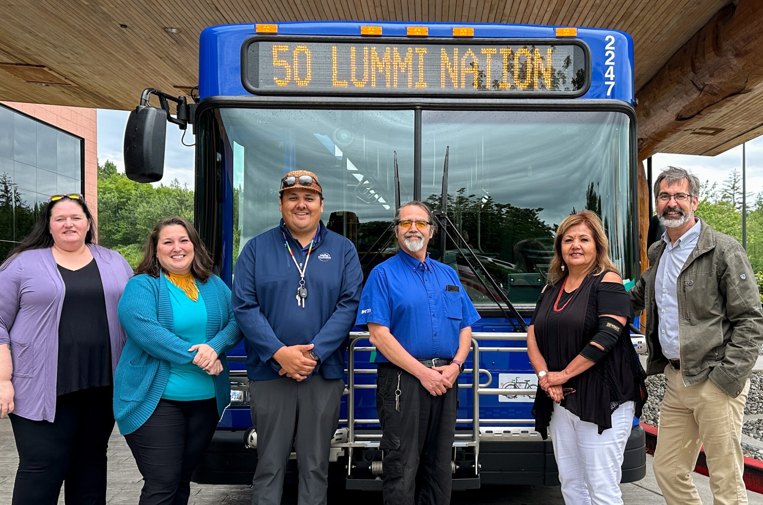 Photo of 6 people standing in front of a bus. the bus says "Route 50 Lummi Nation" and the people are representatives from Whatcom Transportation Authority and Lummi Nation leadership