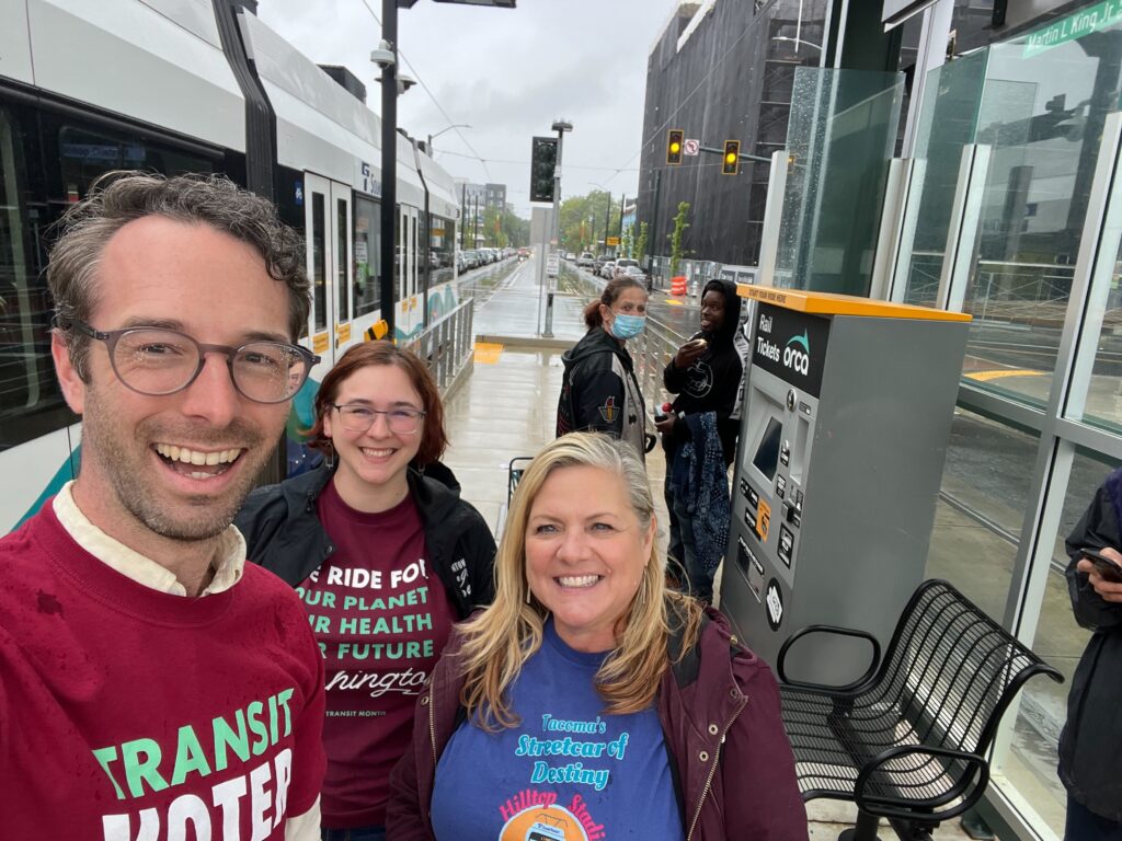 Three people in transit t-shirts take a selfie at a Link light rail platform