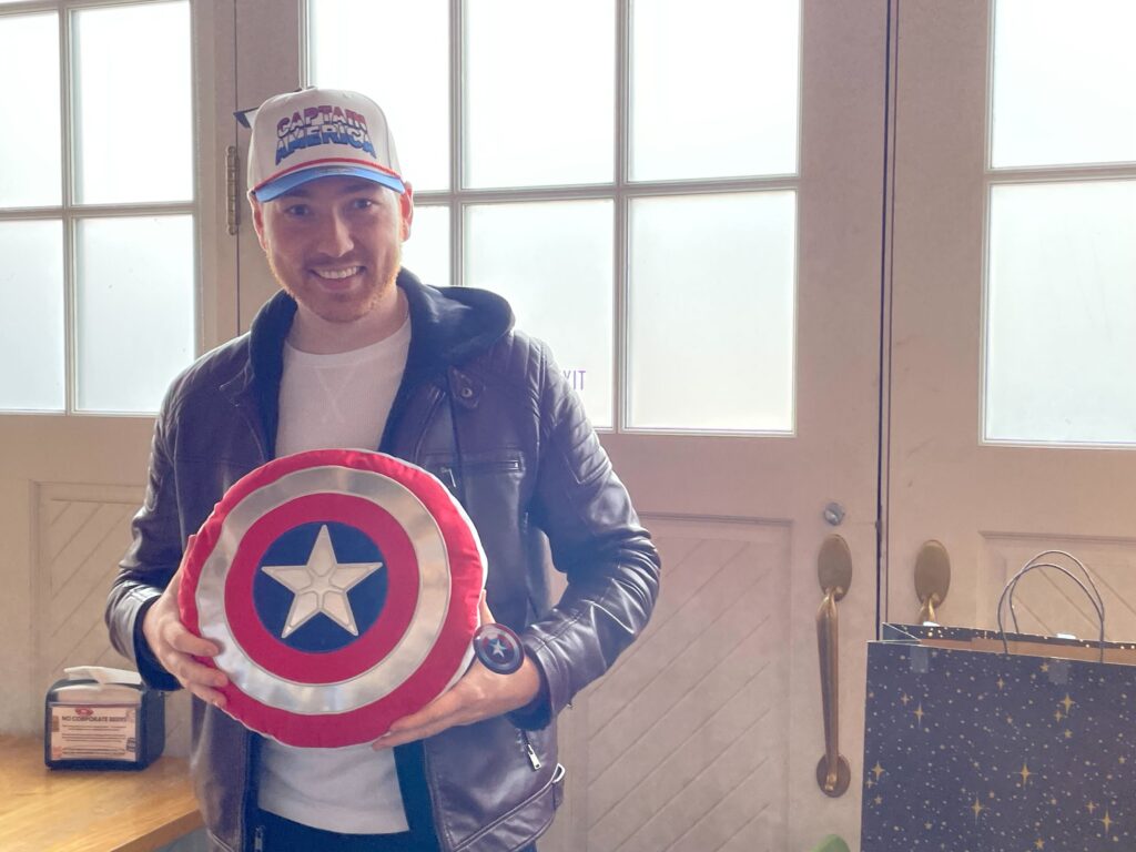 Matthew Sutherland wears a Captain America hat and holds a Captain America shield (pillow). 