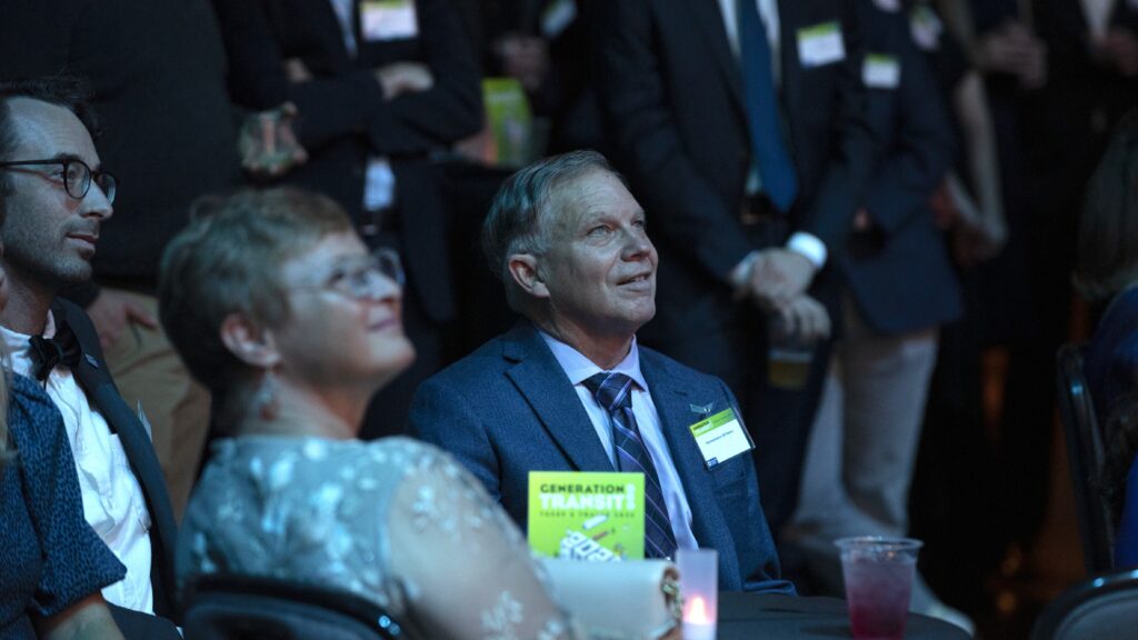 A man seated at a table looks up at a stage.