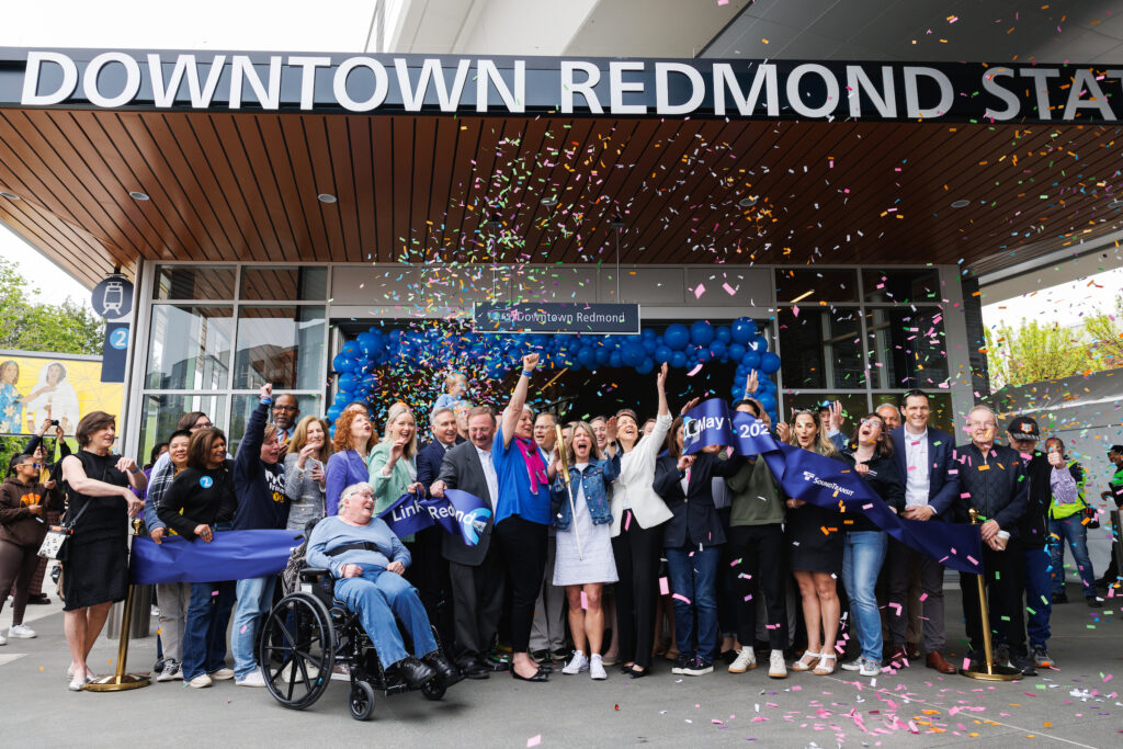 Confetti flies over the heads of a large gathering of public officials as they cut the ribbon on the Downtown Redmond light rail station.