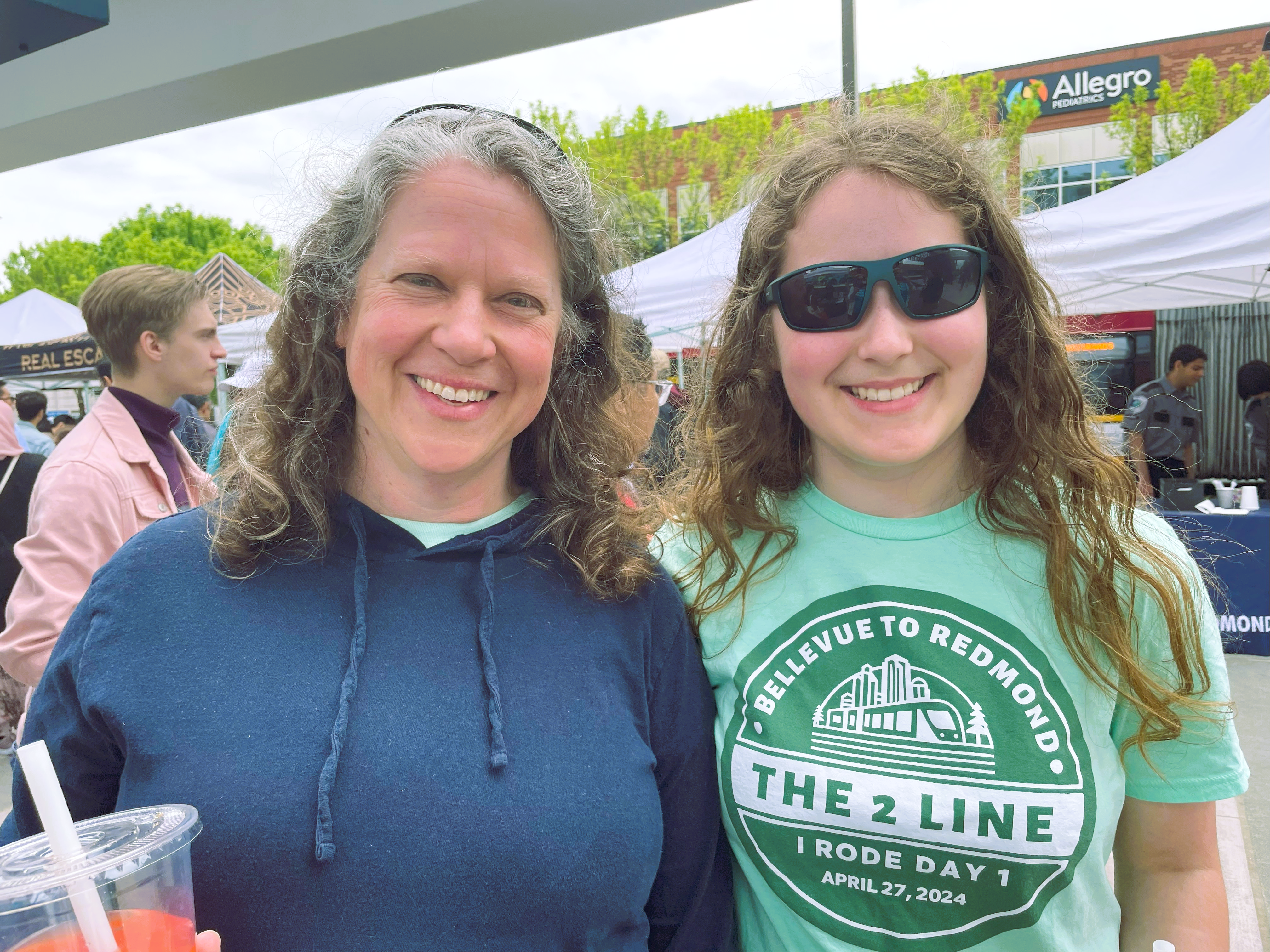 ElizabethAndSarah-Downtown-Redmond A middle aged woman and her daughter smile for the camera. The daughter wears a "2 Line" t-shirt.