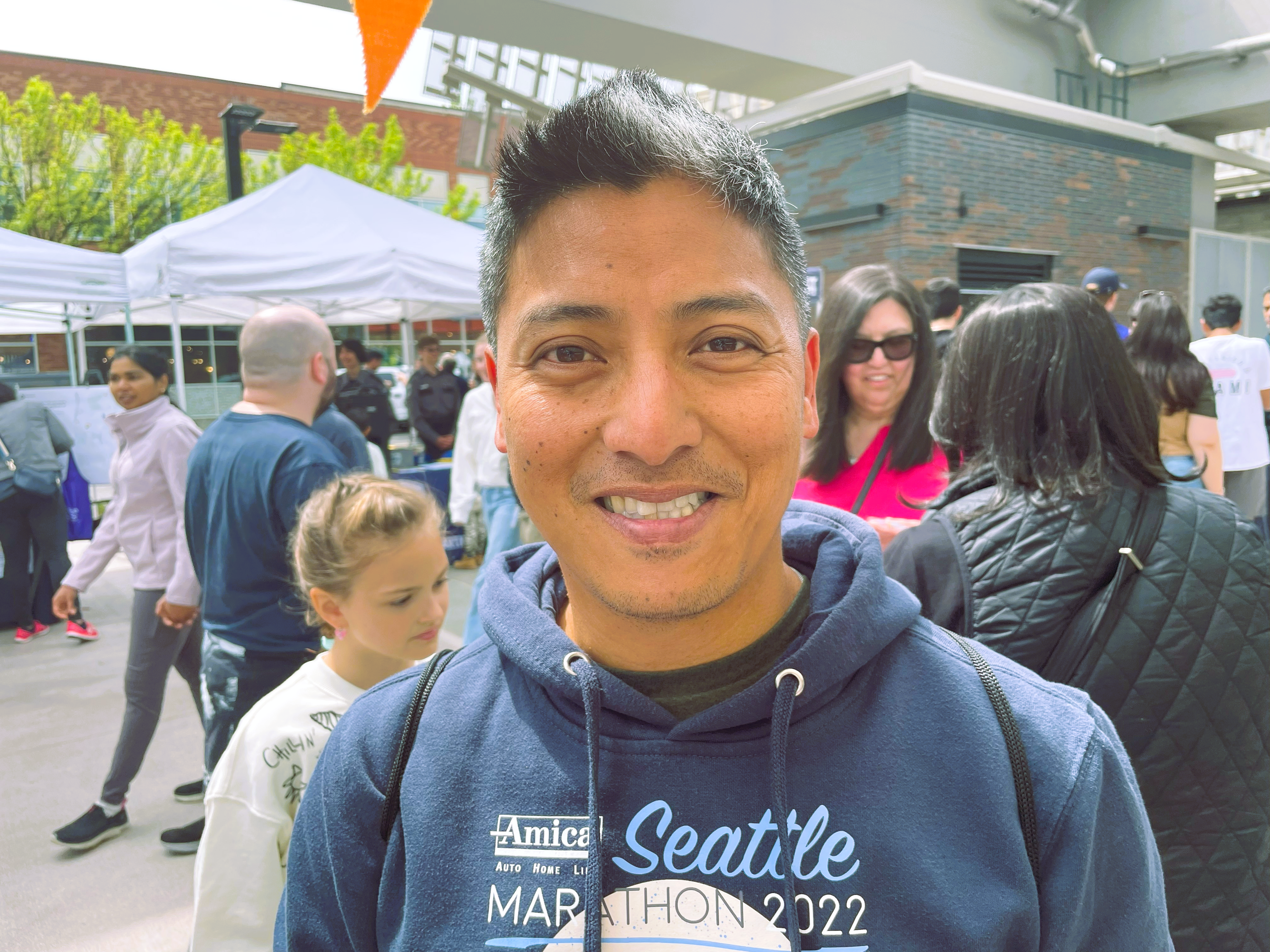 Norberto-Downtown-Redmond A man in a Seattle Marathon 2022 sweatshirt smiles for the camera.