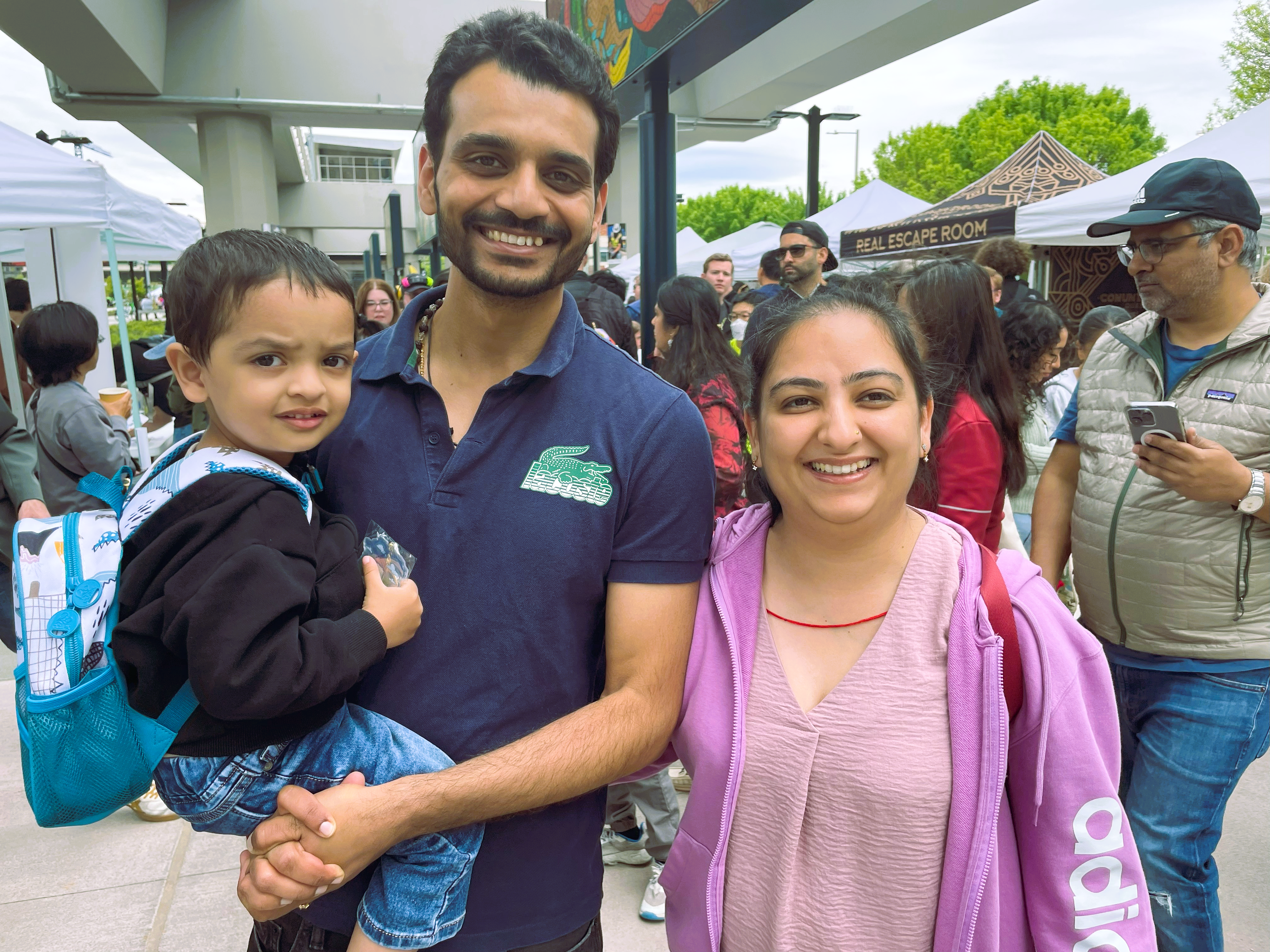 TejaswiFamily-Downtown-Redmond A family of three (man, woman, and toddler) smile for the camera.