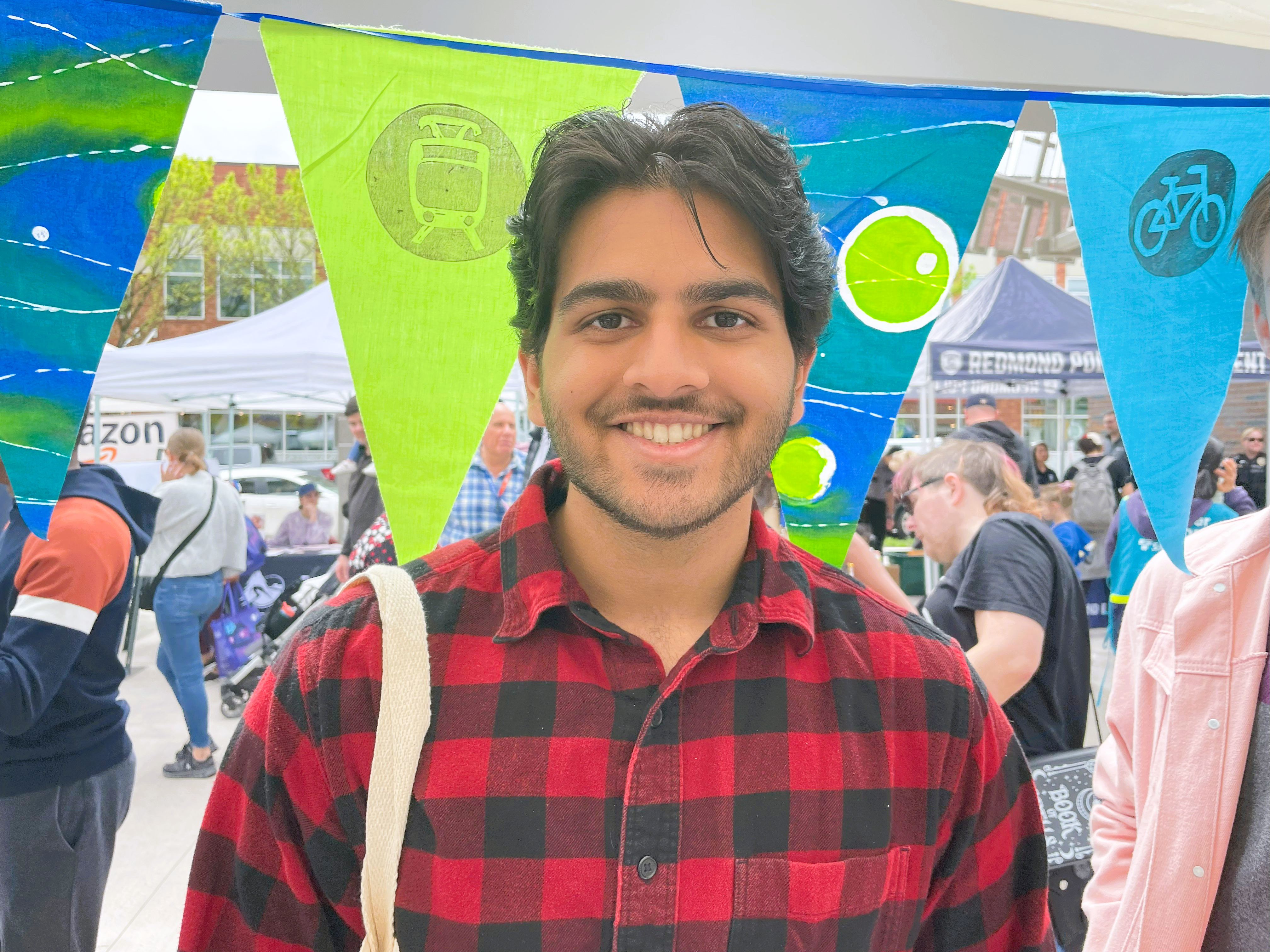 Vivek-Downtown-Redmond A man in a red plaid shirt stands smiling in front of blue and green decorative flags.