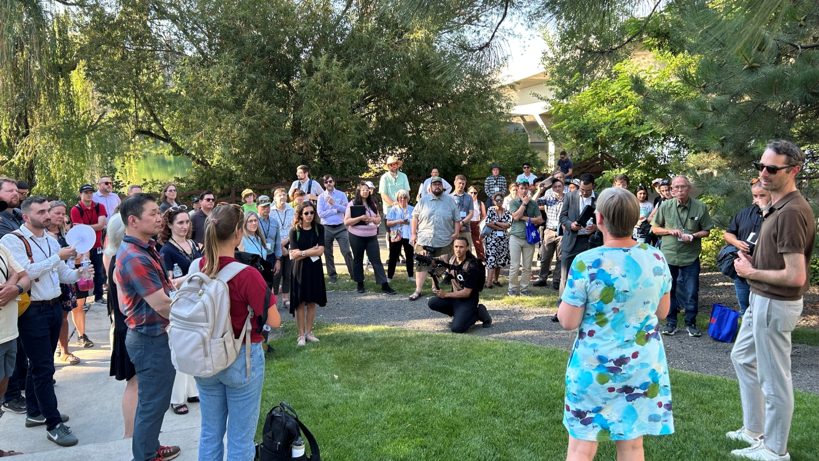 Crowd of people stand outside listening to a speaker.