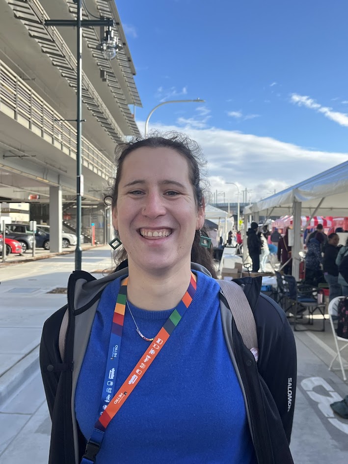 A smiling woman in a blue shirt and black hoodie