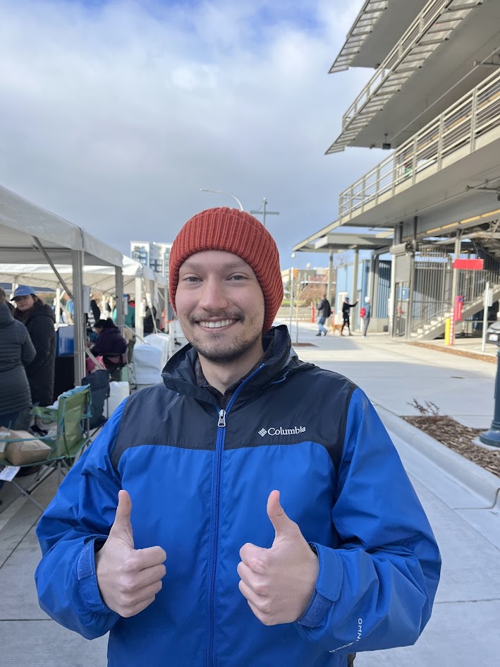 A man in a blue jacket and red had gives two thumbs up