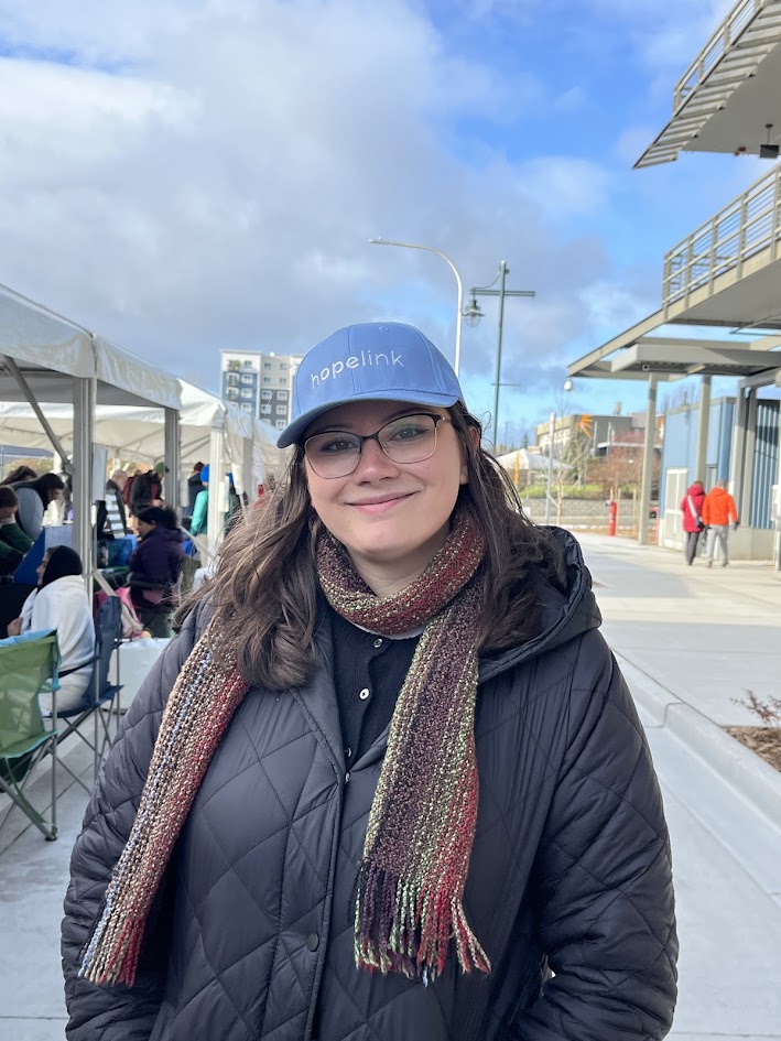A smiling woman in a black jacket with a red-brown scarf and blue 