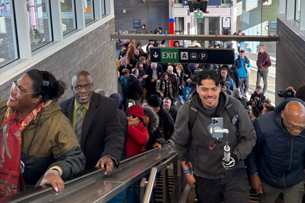 Transit riders ascend stairs and an escalator to ride the train at Federal Way.