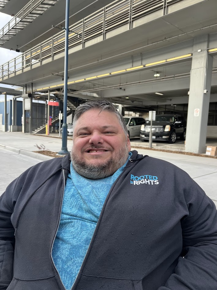 Photo of a smiling man in a hoodie that says "Rooted in Rights"