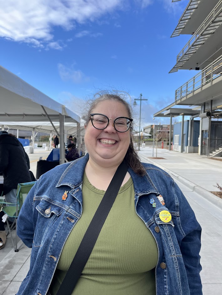 A smiling woman with glasses in a green shirt and blue jean jacket. 