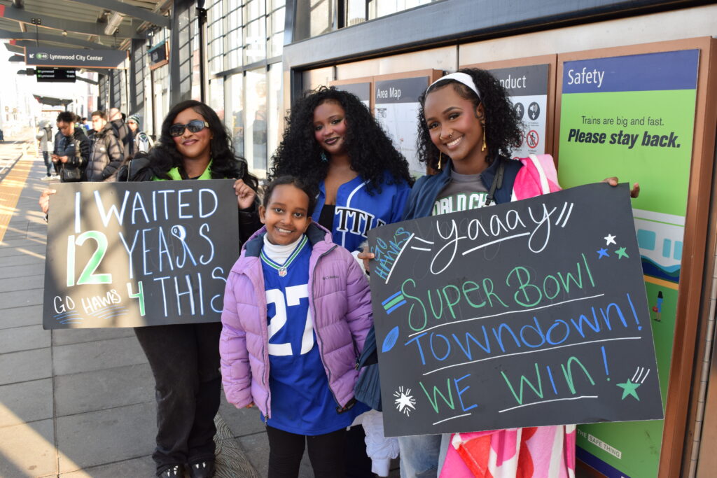 Three women and a young girl wait for the light rail holding signs celebrating the Seahawks victory. 