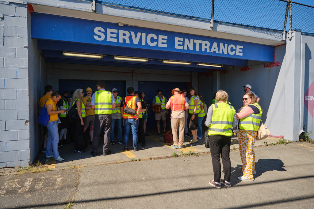 A group of people in safety vests gather in a parking garage entrance.